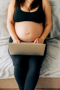 Midsection of woman using digital tablet while sitting on sofa at home