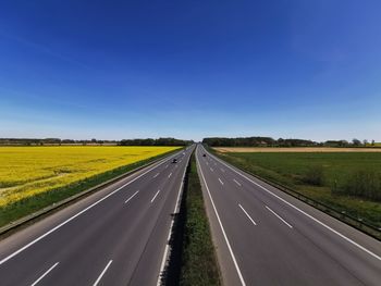 Road amidst yellow field against clear sky