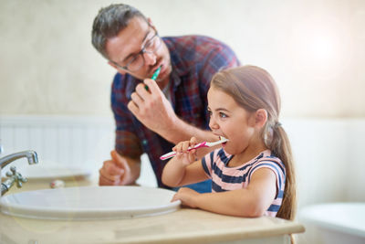 Father and daughter brushing teeth in bathroom