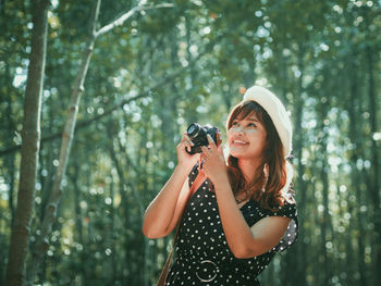 Smiling woman with camera standing in forest