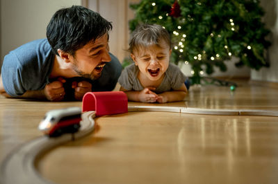 Cheerful father and son playing with toy train at home