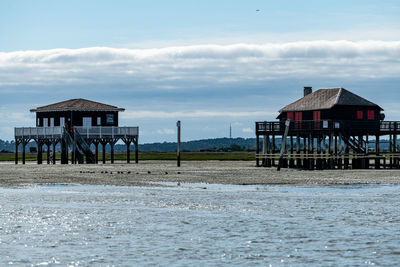 Stilt house by sea against sky