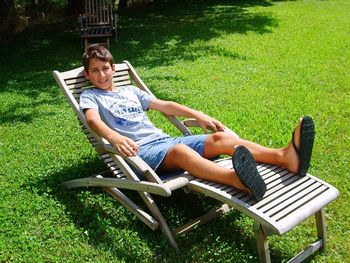Full length portrait of boy relaxing on lounge chair at lawn during sunny day