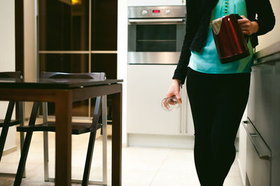 Midsection of woman holding glass and jug while standing at home