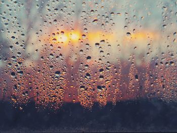 Close-up of wet window against sky during sunset
