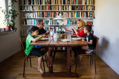 Family having meal at table by bookshelf