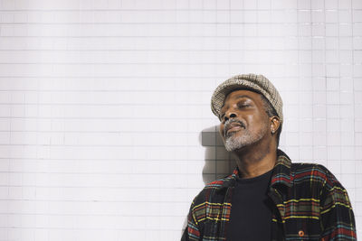 Mature man with eyes closed standing against wall during sunny day