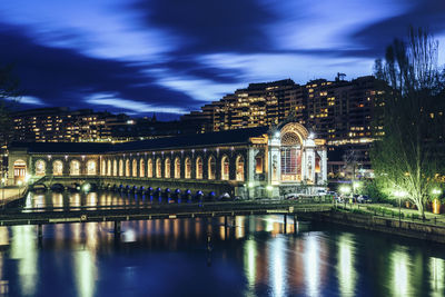 Illuminated bridge over river against cloudy sky
