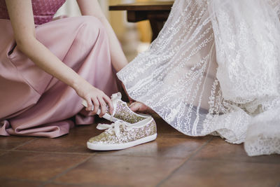 Midsection of friend helping bride put on shoes