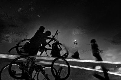 Reflection of silhouette children riding bicycle on puddle
