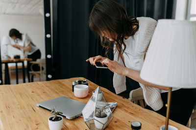 Woman holding mobile phone while standing on table