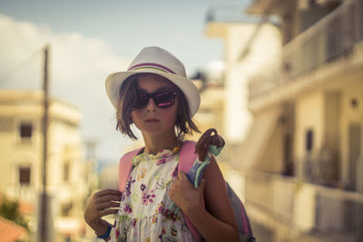 Girl wearing sunglasses standing against sky in city