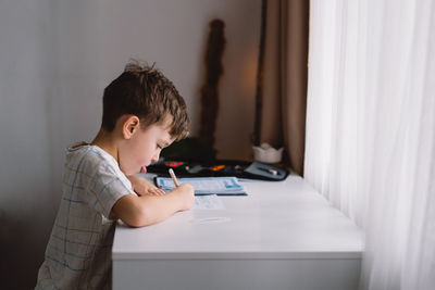 Cute kid boy studying at home and doing school homework. thinking child sitting at table.