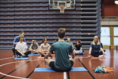 Male coach teaching exercise to students in sports court