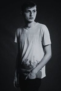 Portrait of young man standing against black background