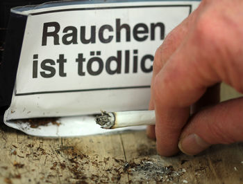 Close-up of hand smoking cigarette with text on table