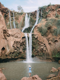 Rear view of woman standing on rock against waterfall