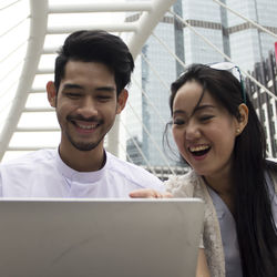 Close-up of smiling friends using laptop in city