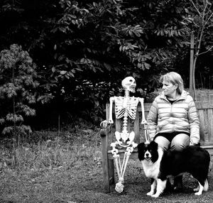 Woman sitting by human skeleton on bench at park