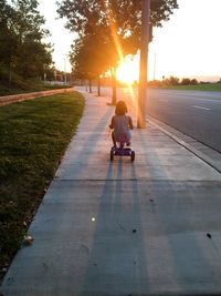 Rear view of girl riding tricycle on footpath at sunset