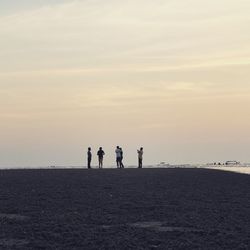 Friends standing at beach against sky during sunset
