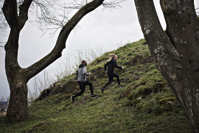 Full length of multi-ethnic couple jogging on hill in forest