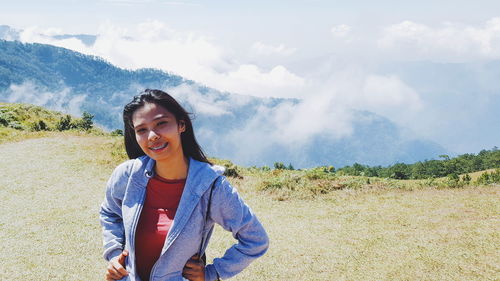 Portrait of smiling young woman standing on field against sky