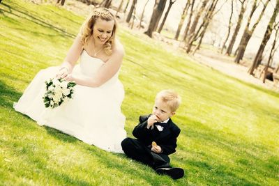 Happy bride looking at boy while crouching on grassy field