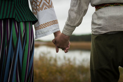 Midsection of couple holding hands while standing at lakeshore