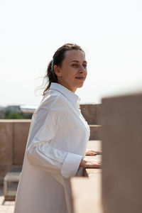 Side view of young woman standing against sky