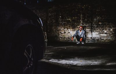 Man wearing sunglasses sitting by wall outdoors