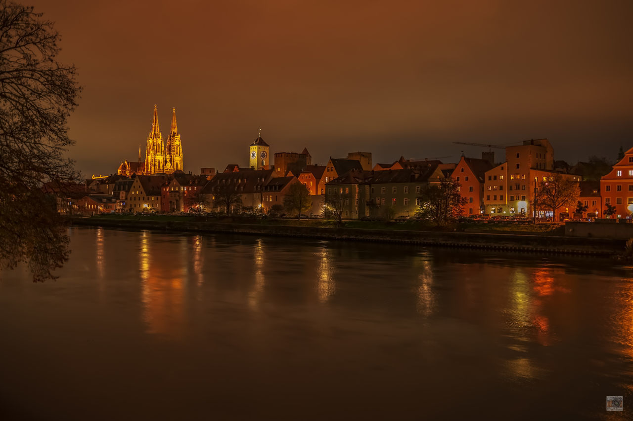 ILLUMINATED BUILDINGS BY RIVER AGAINST SKY IN CITY