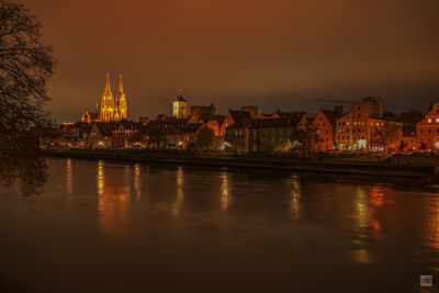 Illuminated buildings by river against sky in city at night