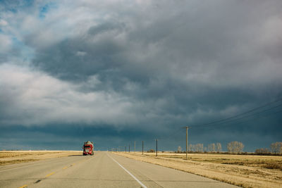 Truck moving on road against cloudy sky