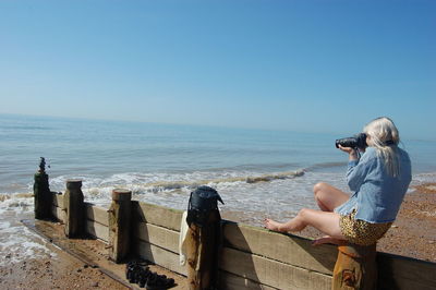 Lady photographing on sea against sky