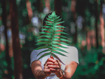 Close-up portrait of young woman holding plant standing outdoors