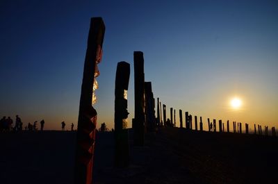 Silhouette wooden posts on beach against clear sky during sunset