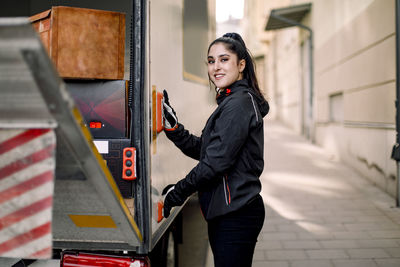 Side view portrait of young delivery woman with truck in city