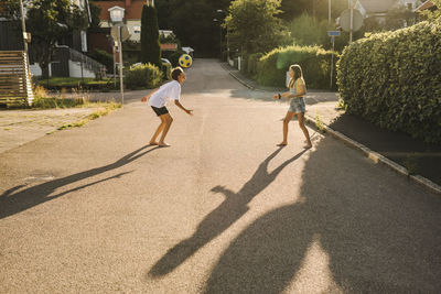 Siblings playing with soccer ball on road during sunny day