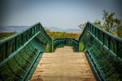 Footbridge amidst trees against sky
