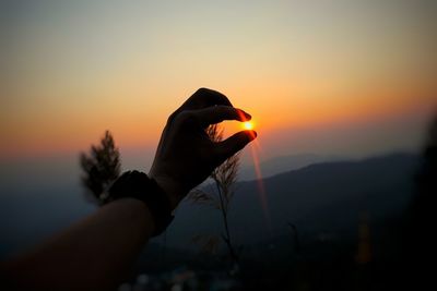 Silhouette person holding orange against sky during sunset