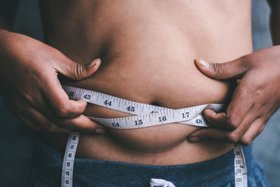 Midsection of woman measuring her waist with tape measure