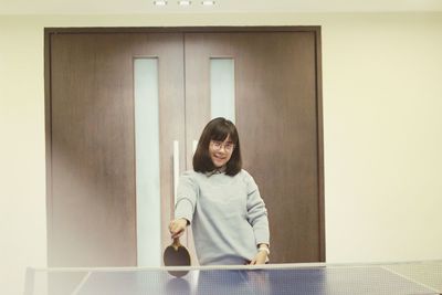 Portrait of young woman holding table tennis racket at home