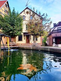 House by lake and buildings against sky