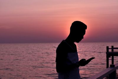 Man using phone by sea during sunset