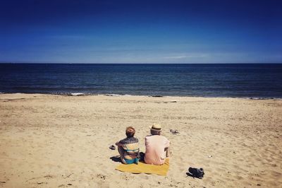 Rear view of couple sitting on beach against clear sky