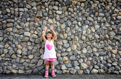 Cute girl standing on street against stone wall