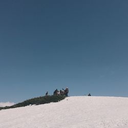 People on sand dune against clear blue sky
