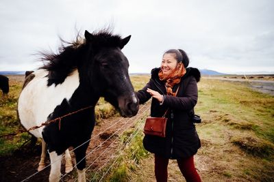 Smiling woman petting horse on field