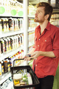 Man holding mobile phone while shopping at refrigerated section in supermarket